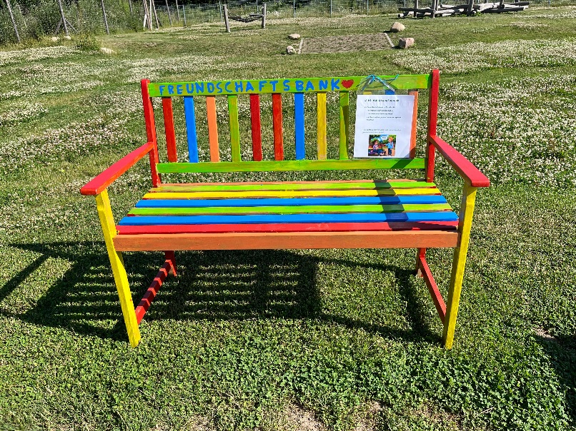 Eine bunte Holzbank mit der Aufschrift 'Freundschaftsbank' auf Rasen